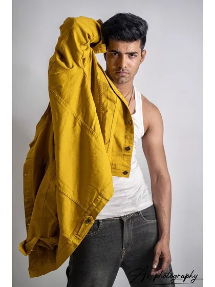 A studio shot of a model holding a yellow denim jacket over his shoulder. This pose creates a dynamic and edgy look, highlighting the jacket as the key piece in this fashion photography session.
