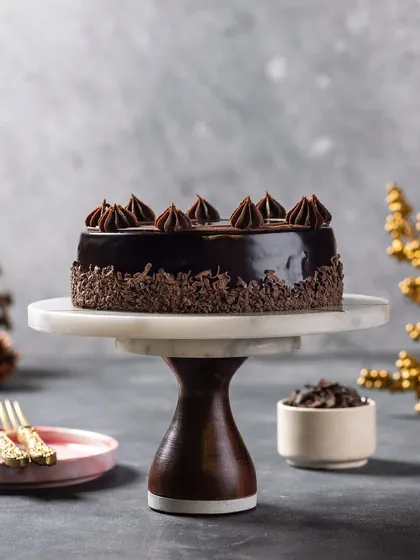 A rich chocolate truffle cake on a marble and wood cake stand. The blurred background and focused lighting create a sophisticated mood.