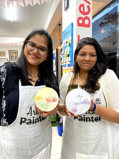 Two friends with their finished wood slice paintings. This unique surface adds a natural and rustic feel to the artwork.