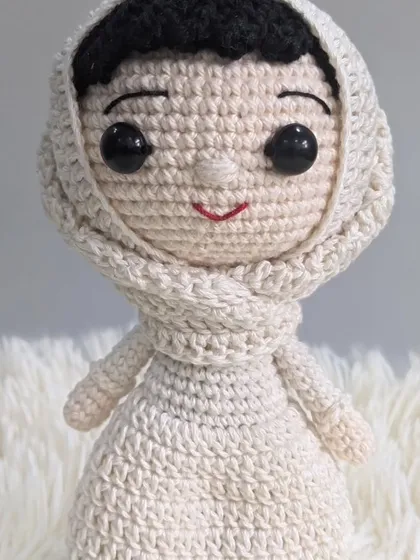 A close-up of a custom female doll with a headscarf, showcasing the gentle smile and detailed stitching.