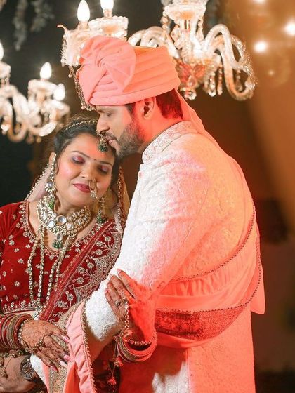A tender and emotional moment between the couple on their wedding day, captured under the soft light of a chandelier.