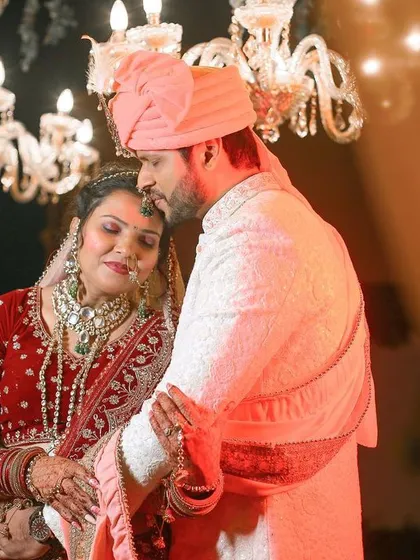 A tender and emotional moment between the couple on their wedding day, captured under the soft light of a chandelier.