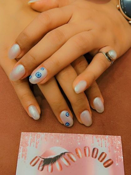 A trendy and protective design on short, oval nails. The pearly white base is adorned with hand-painted evil eye symbols on the ring fingers.