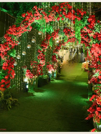 A pathway of passion. This entrance arch is covered in vibrant red roses and greenery, with hanging lanterns adding a soft glow, creating a romantic and dramatic welcome.