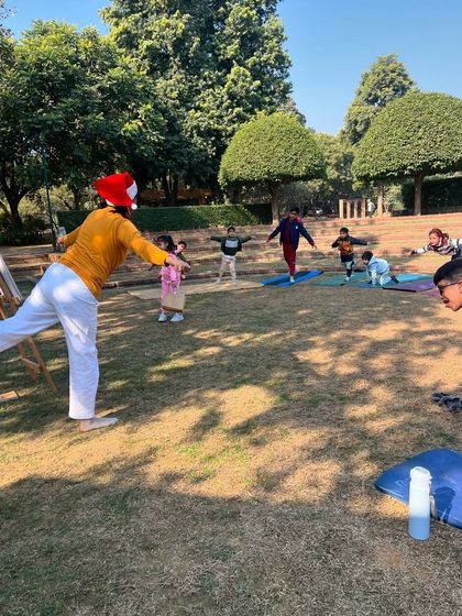 A teacher wearing a Santa hat leads a group of children in an outdoor yoga class. We love to combine the fun of festivals with the discipline of yoga.
