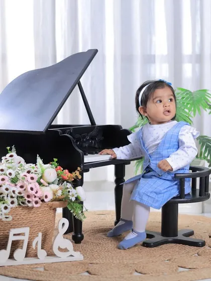 A sweet moment at the piano. This little musician is seated comfortably for her first birthday portrait, creating a charming and classic scene.
