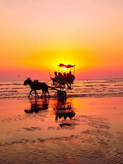 A beautifully composed shot of a horse-drawn carriage silhouetted against a vibrant sunset on Alibaug beach, with its reflection on the wet sand.