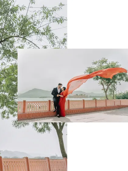 An artistic composition of a couple by the lake, with the flowing red saree framed by green leaves.