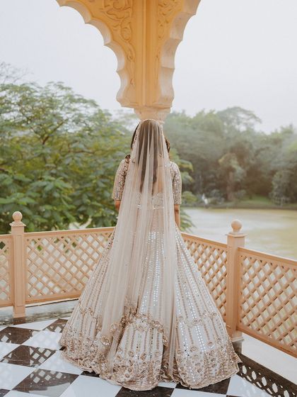 A bride stands on a balcony overlooking a lake, her long veil trailing behind her, creating a sense of quiet contemplation.