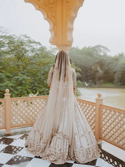 A bride stands on a balcony overlooking a lake, her long veil trailing behind her, creating a sense of quiet contemplation.