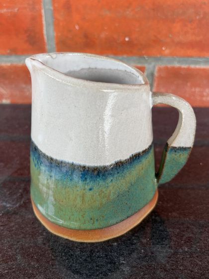 A lovely handmade milk pitcher with a beautiful glaze that transitions from white to green and blue. It's the perfect size for serving cream or milk with your morning coffee or tea.