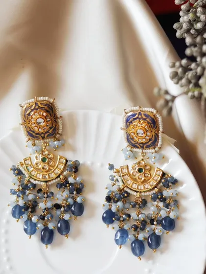 These ornate blue earrings are set against a simple white plate and soft silk. This contrast allows the intricate Meenakari work and delicate bead clusters to stand out, creating a look of pure elegance.
