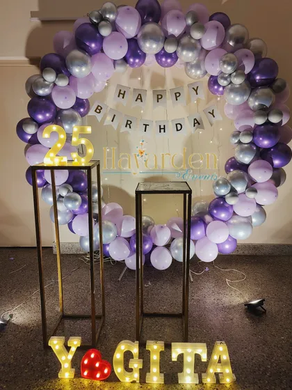 A purple and silver themed 25th birthday. The decor features a full balloon ring, marquee numbers on pedestals, and light-up letters for the name.