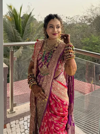 A bride in a pink and purple Paithani, posing on a balcony.