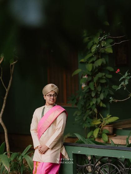 The groom, in his wedding attire, stands on the verandah, surrounded by lush greenery.