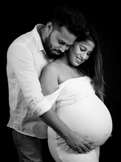 A beautiful black and white close-up. The partner embraces the mom-to-be from behind, both looking down at the baby bump in a moment of shared love.