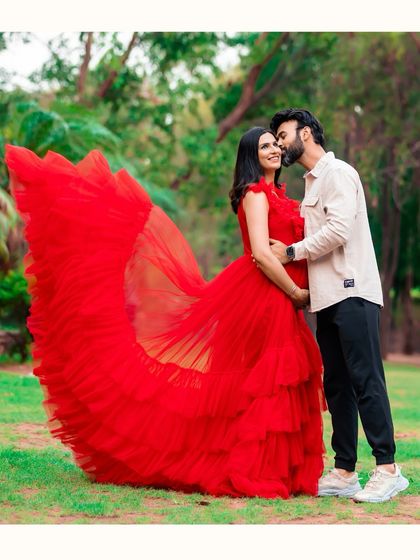 A romantic kiss on the cheek shared between a couple during their outdoor photoshoot. The vibrant red of the gown flows beautifully, adding a dramatic and passionate feel to the image.