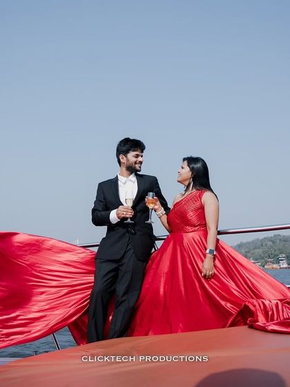 A couple shares a toast on a yacht in Goa, her brilliant red gown creating a stunning visual against the open water, perfect for a luxury pre-wedding shoot.