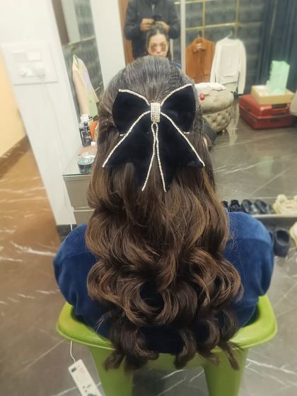 A glamorous party look with a half-up style, deep waves, and a statement black velvet bow with crystal tassels. This accessory adds a touch of modern drama.