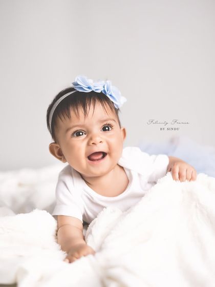 A happy baby girl enjoying tummy time on a soft white blanket. Her bright smile and the simple, clean background create a classic and timeless portrait.