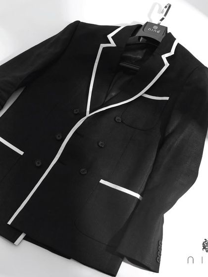 The black double-breasted blazer with white piping, laid flat to showcase its structure and design. A truly timeless piece.