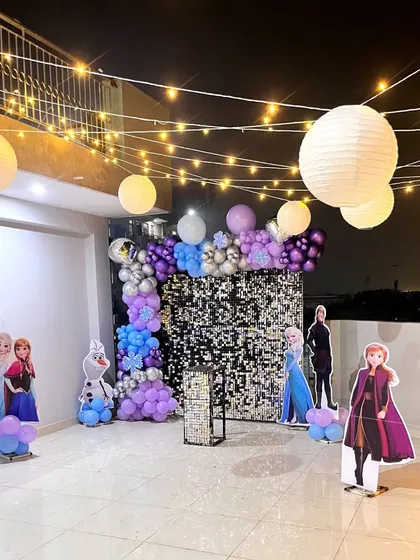 I bring popular kids' themes to life, like this spectacular Frozen-themed party on a terrace. The setup includes a silver sequin wall, a balloon arch in shades of purple and blue, character cutouts of Elsa, Anna, and Olaf, and beautiful paper lanterns for a magical evening glow.