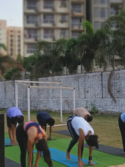 A group of athletes at our Kanjurmarg park location work on a standing forward bend, a classic yoga pose to lengthen the entire backside of the body.