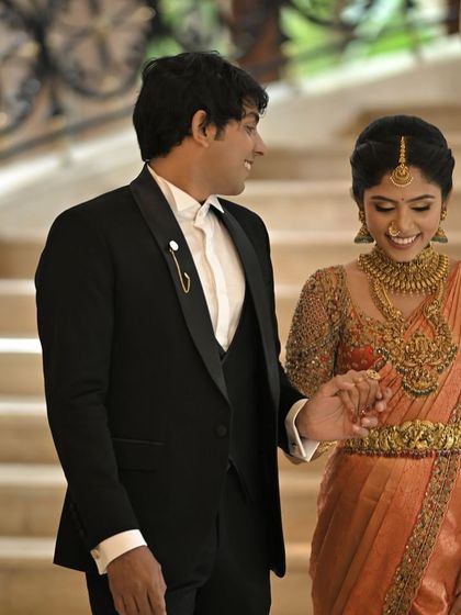 A beautiful moment between the bride and groom. Her custom orange silk saree and his classic black tuxedo show how I design for couples, ensuring their looks are coordinated and equally special.