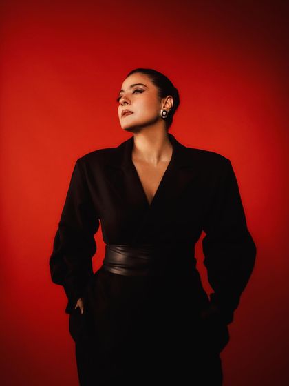 Another powerful pose against the red backdrop, emphasizing the strong silhouette of the black dress.