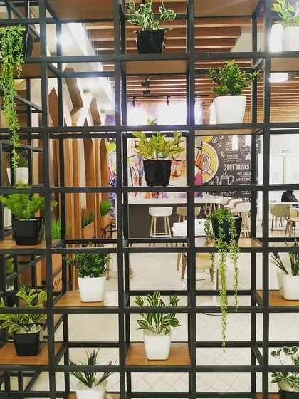 In this restaurant project, I used a custom black metal grid shelf as a stylish divider. By filling it with a variety of small potted plants and hanging vines, it separates the space while maintaining an open, airy, and green atmosphere.