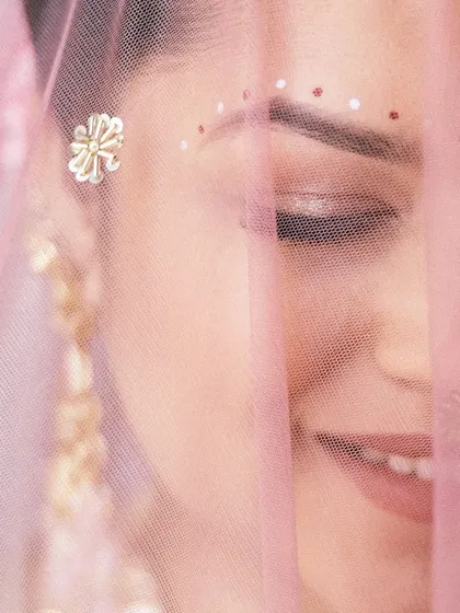 A beautiful close-up of the bride, seen through her delicate pink veil. Her gentle smile and the traditional bindi art create a soft, romantic, and culturally rich portrait.