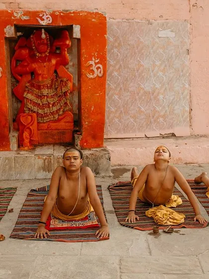 Young Batuks practice yoga poses in front of a shrine. This image shows how physical discipline is integrated into their spiritual training from a young age.