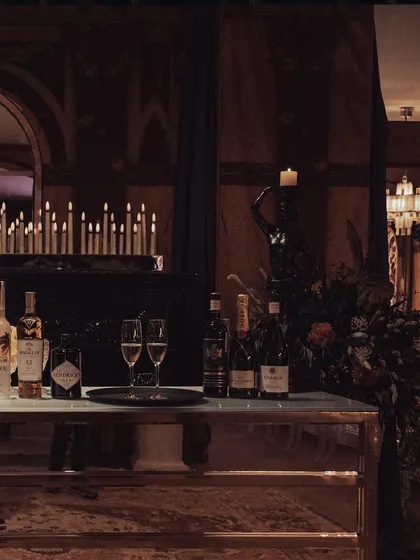A moody shot of the bar setup for the Versailles event, featuring premium spirits and champagne against a backdrop of dozens of candles. The atmosphere is one of classic, opulent luxury.