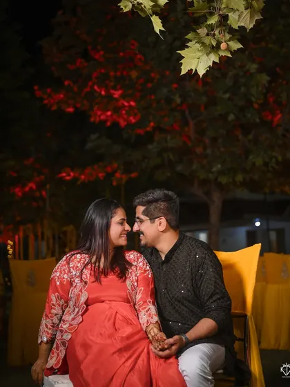 A romantic evening shot of the couple during their Mehandi function, framed by beautiful red leaves and bokeh lights.