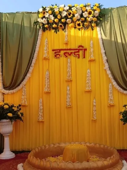 This is a classic Haldi ceremony backdrop I created for an outdoor event. The setup uses a bright yellow fabric base with contrasting green drapes, and the top is decorated with fresh sunflowers and white chrysanthemums for a vibrant look.