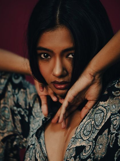 A powerful and engaging shot where the model's hands create a frame around her face. Her direct gaze is captivating, and the composition is tight and focused. This image has a strong, confident energy.