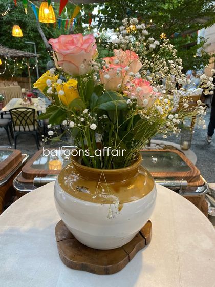 A close-up of a rustic floral centerpiece used in the 'Oh Babies' baby shower, featuring pink and yellow roses in a traditional pot.