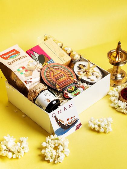 The 'Jamanthi Poo' Onam hamper, a bright and cheerful collection. It includes sweet and savory treats, a scented candle, and a Kathakali magnet, all set against a vibrant yellow backdrop symbolizing prosperity.