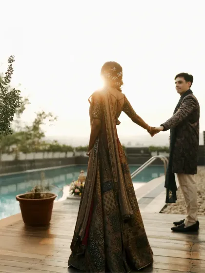 A beautiful backlit shot of the couple by the pool. The groom leads the bride, creating a sense of a shared journey beginning.