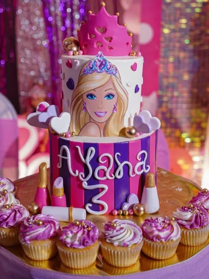 Bring the glamour to your party with a custom Barbie-themed cake. This two-tiered creation features a portrait of Barbie, a fondant crown, and matching cupcakes, perfect for a fan's birthday.