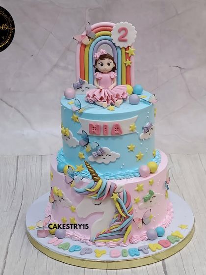 This two-tier unicorn cake is a fairytale dream. The choco-vanilla cake features a sweet girl figurine under a rainbow on top, with a 2D unicorn, butterflies, and stars decorating the pink and blue tiers.