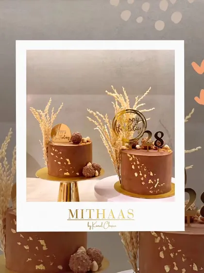 Two beautiful chocolate cakes ready for a celebration. Both are decorated with gold leaf and custom toppers, with one featuring Ferrero Rochers and the other a "28" for a birthday.