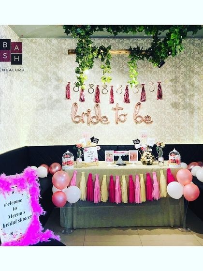 This is the full view of a bridal shower welcome area and decor table. A personalized sign greets guests, leading them to a decorated space with balloons, tassels, and props for the celebration.