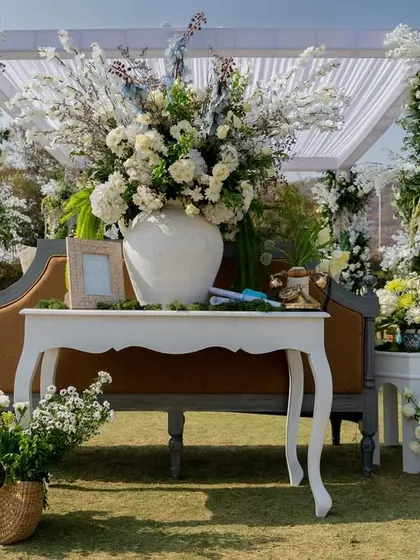 A chic seating area at the white and green Haldi, with a vintage-style bench and console table adorned with massive floral arrangements.