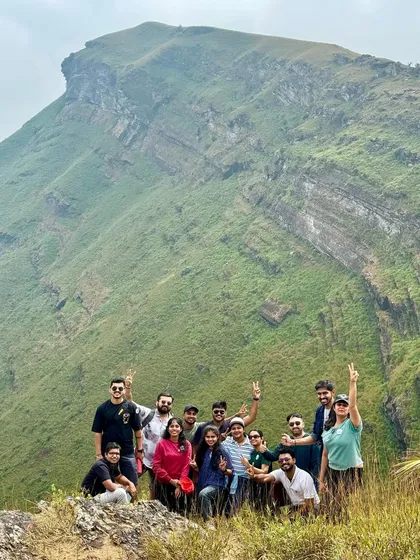 A group celebrating their climb with a stunning mountain cliff in the background. These are the views that make the effort of a trek completely worthwhile.
