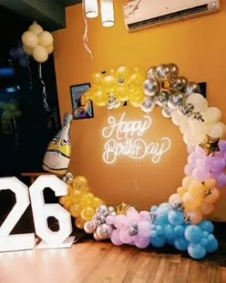 A colorful and fun 26th birthday setup. The circular balloon arch uses a mix of pastel colors with a champagne bottle balloon for a celebratory touch.