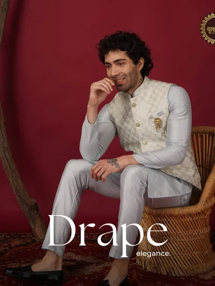Drape elegance. A model seated in a light blue kurta and beige patterned Nehru jacket, looking relaxed and stylish.