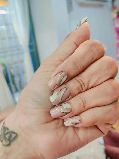 A beautiful and subtle design on natural nails. The nude base is accented with delicate swirls of white and gold glitter.