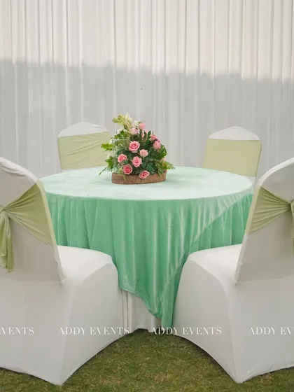 An elegant guest table setup for the Nikah. The pastel green velvet tablecloth is paired with white chair covers and matching green sashes, creating a cohesive and sophisticated look.
