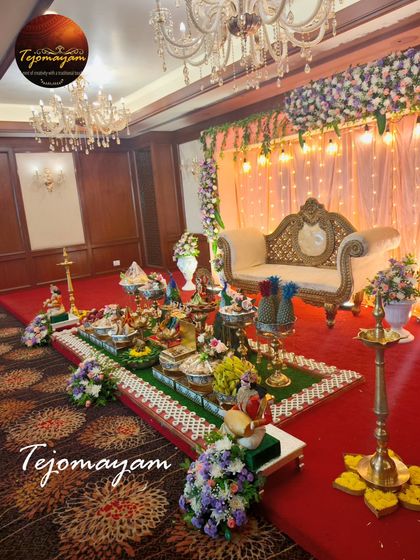 A beautiful half-saree ceremony setup with an elegant floral backdrop and a full display of traditional offering plates.